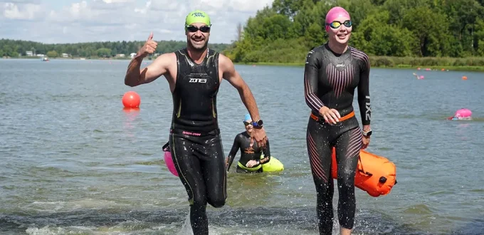 Мужчина и женщина в гидриках выходят из воды. Заплыв на открытой воде Iver Swim